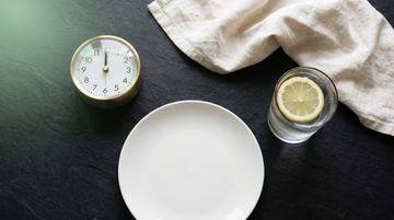 Copo de água com limão e relógio analógico sobre superfície escura — representação visual do jejum intermitente e da janela de alimentação